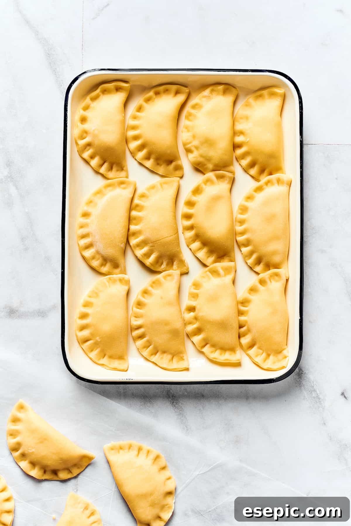 Tray of Freshly Made Uncooked Pierogi A baking sheet filled with perfectly shaped, uncooked homemade pierogi, covered lightly with a towel.