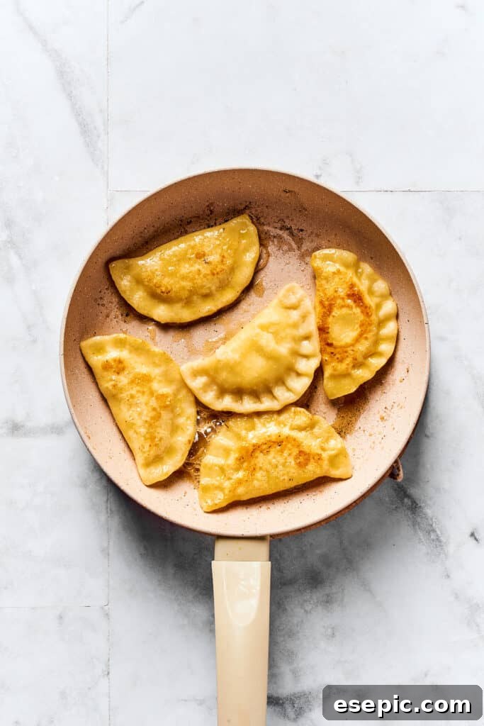 The Ultimate Homemade Pierogi Guide 9 Golden-brown pierogi frying in melted butter in a large skillet, developing a crispy crust.