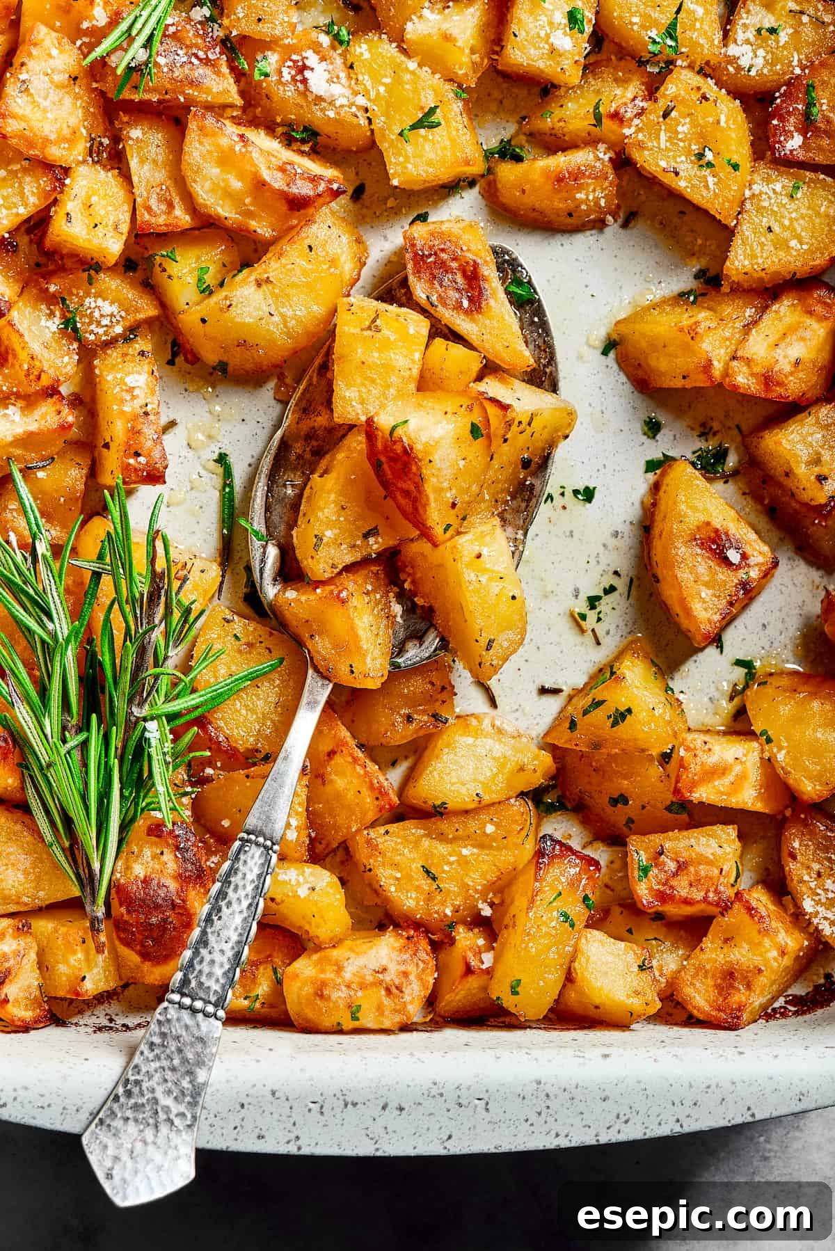 Overhead shot of seasoned baked potato chunks in a baking dish, garnished with fresh rosemary.