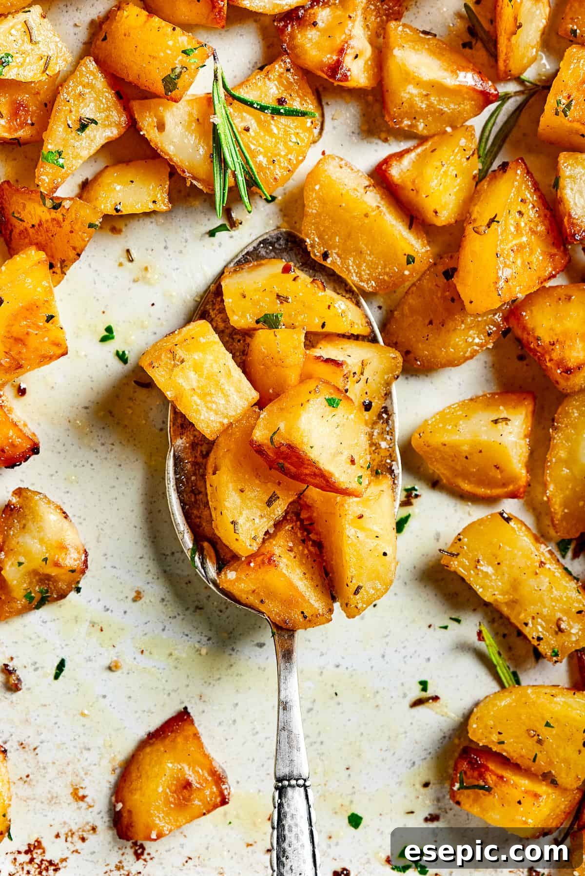 A tray of golden-brown roast potatoes with a silver spoon scooping up some pieces.