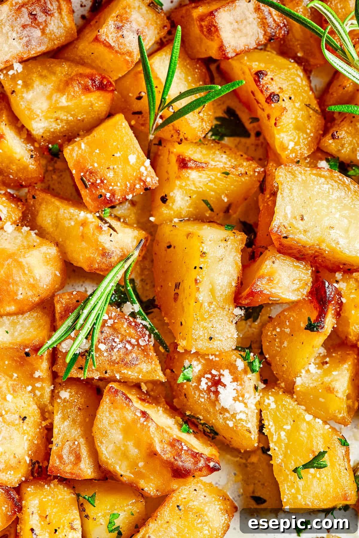 Close-up shot of oven roasted potatoes garnished with fresh rosemary leaves and grated Parmesan cheese.
