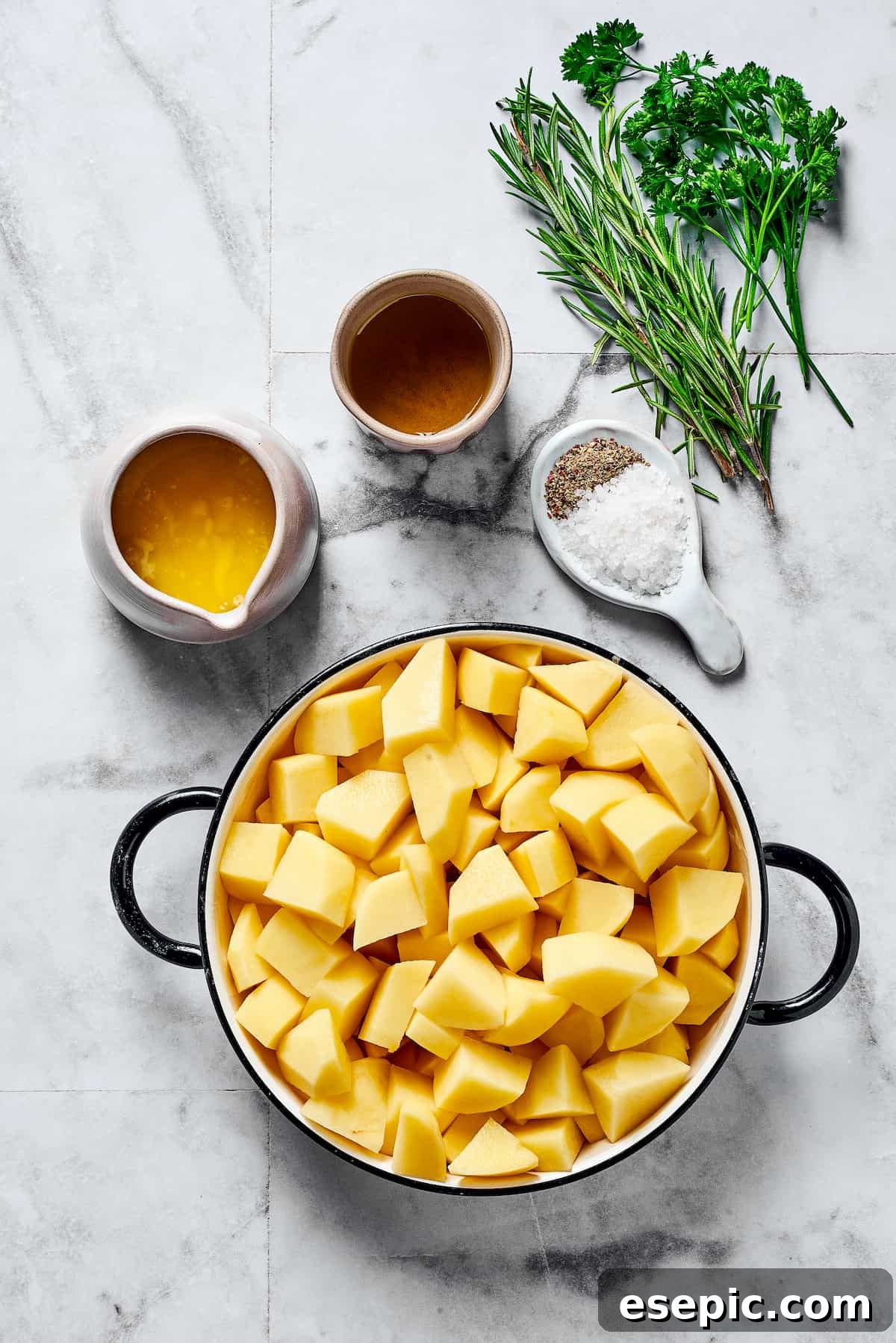 From top: Olive oil, fresh rosemary, fresh parsley, melted butter, salt and pepper, and cut-up raw potatoes, ingredients for seasoning.