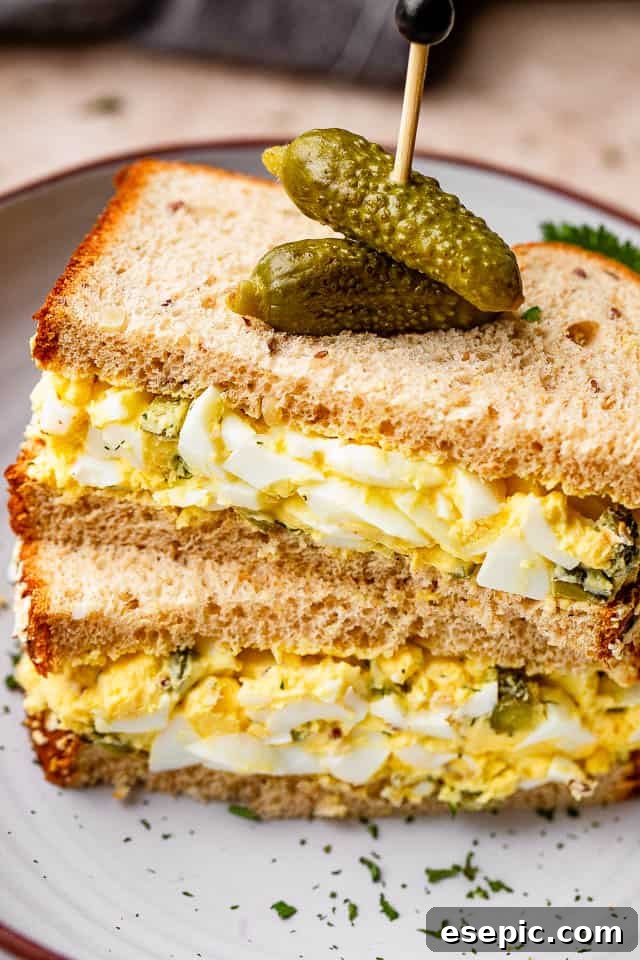 stacked up egg salad sandwich with pickles pinned on top