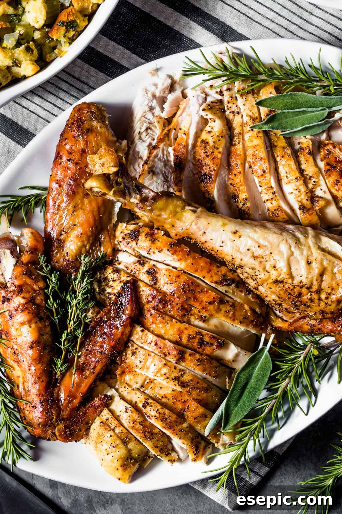 An overhead shot of a carving board displaying a perfectly cooked and sliced roast turkey, accompanied by fresh green herbs.
