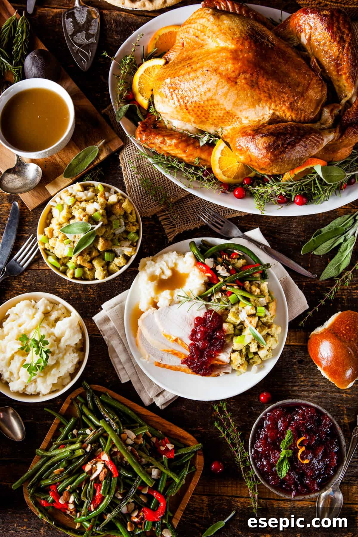 An overhead shot of a full Thanksgiving dinner spread, featuring a whole roasted turkey, mashed potatoes, stuffing, green beans, and cranberry sauce.