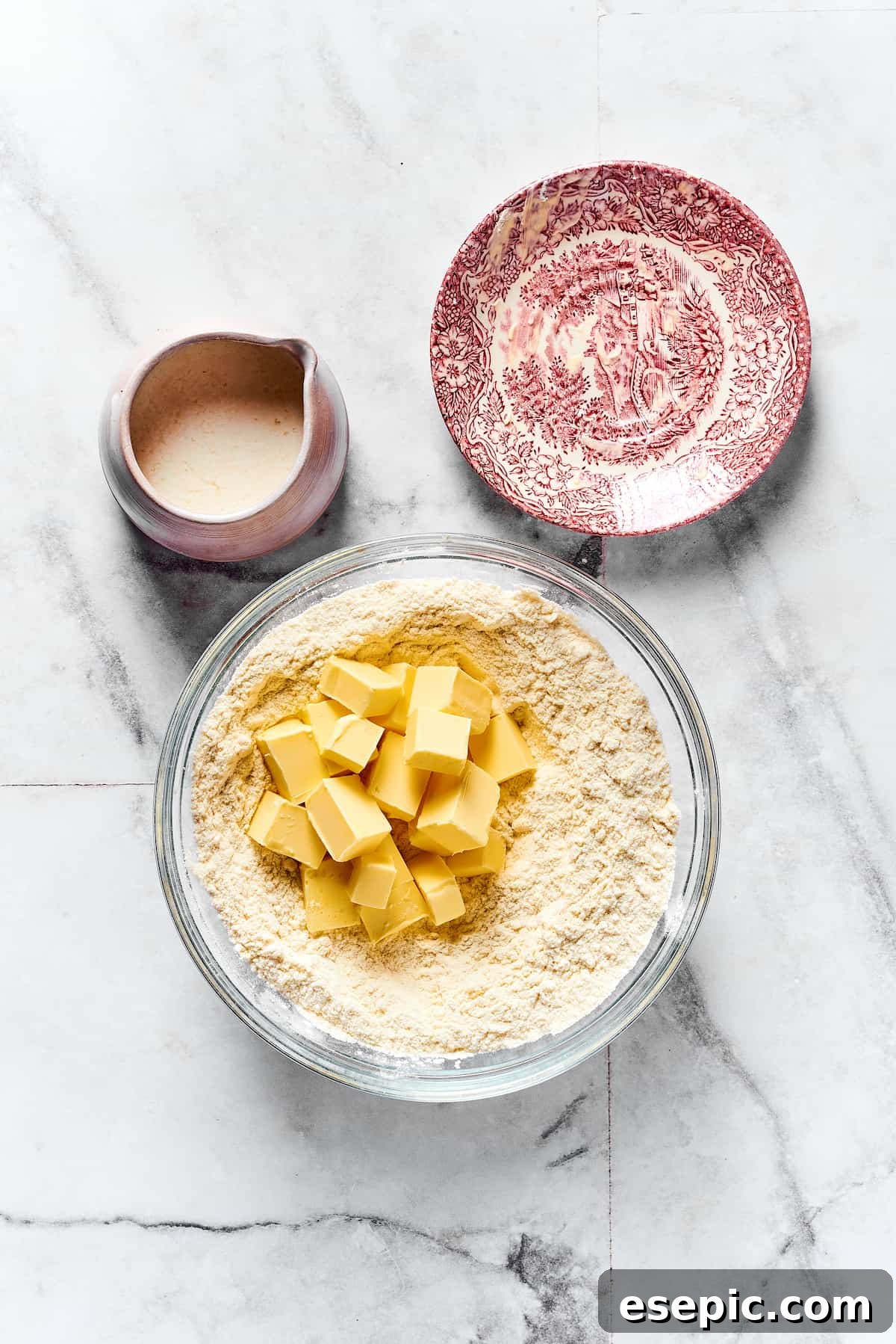 Butter cubes being added to dry ingredients in a mixing bowl.
