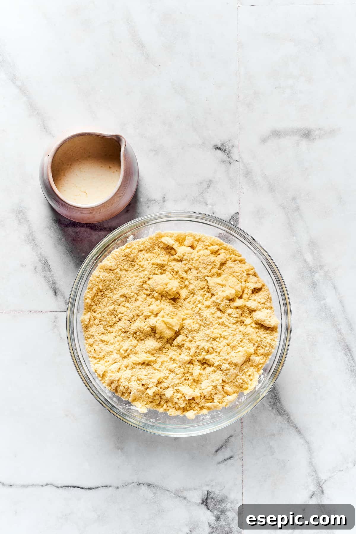 A mixing bowl of dry biscuit ingredients next to a small pitcher of buttermilk.