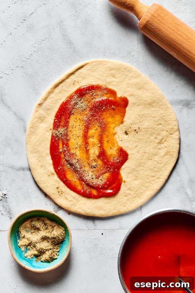 Pizza sauce and seasonings spread on one half of a dough circle.