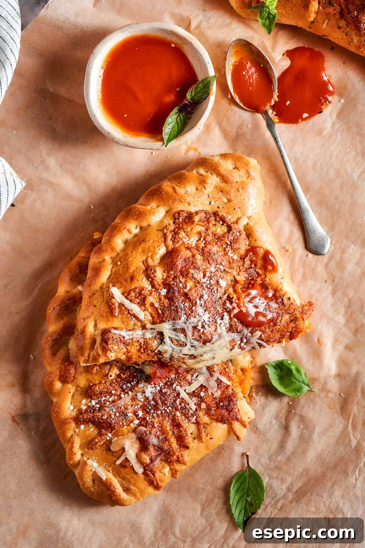 A freshly baked calzone, sliced in half, revealing its rich, cheesy, and pepperoni-filled interior, next to a bowl of marinara dipping sauce.