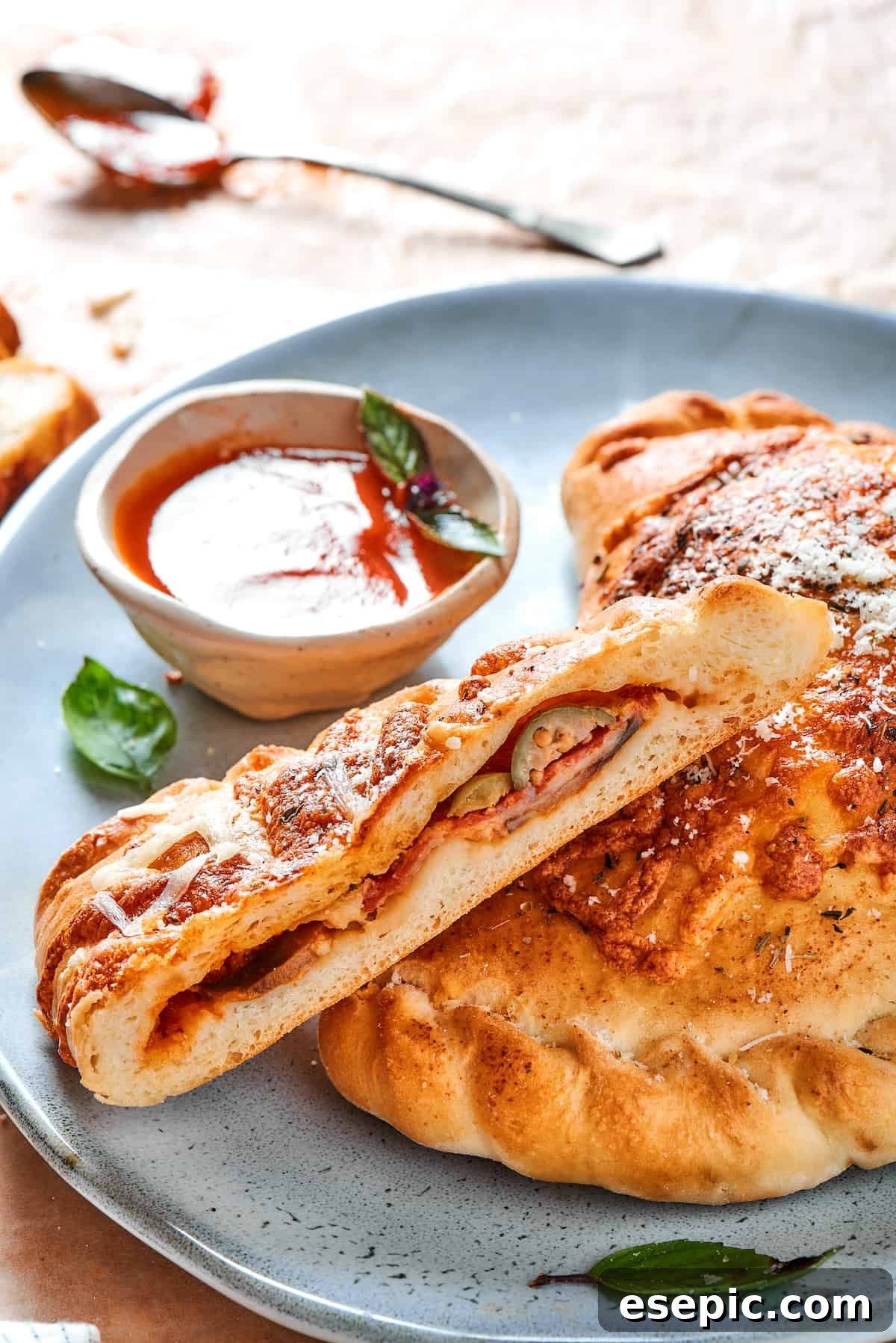 A baked pizza pocket cut in half, revealing its cheesy interior, served on a blue plate with a side of dipping sauce.