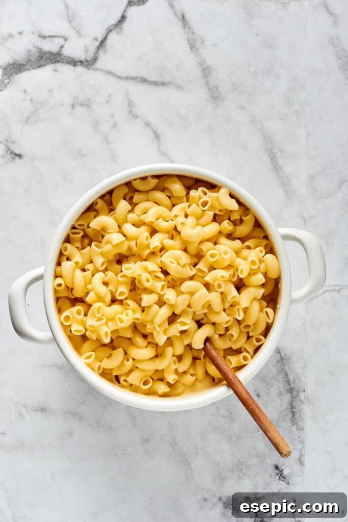 Stirring cooked elbow pasta into cheese sauce.