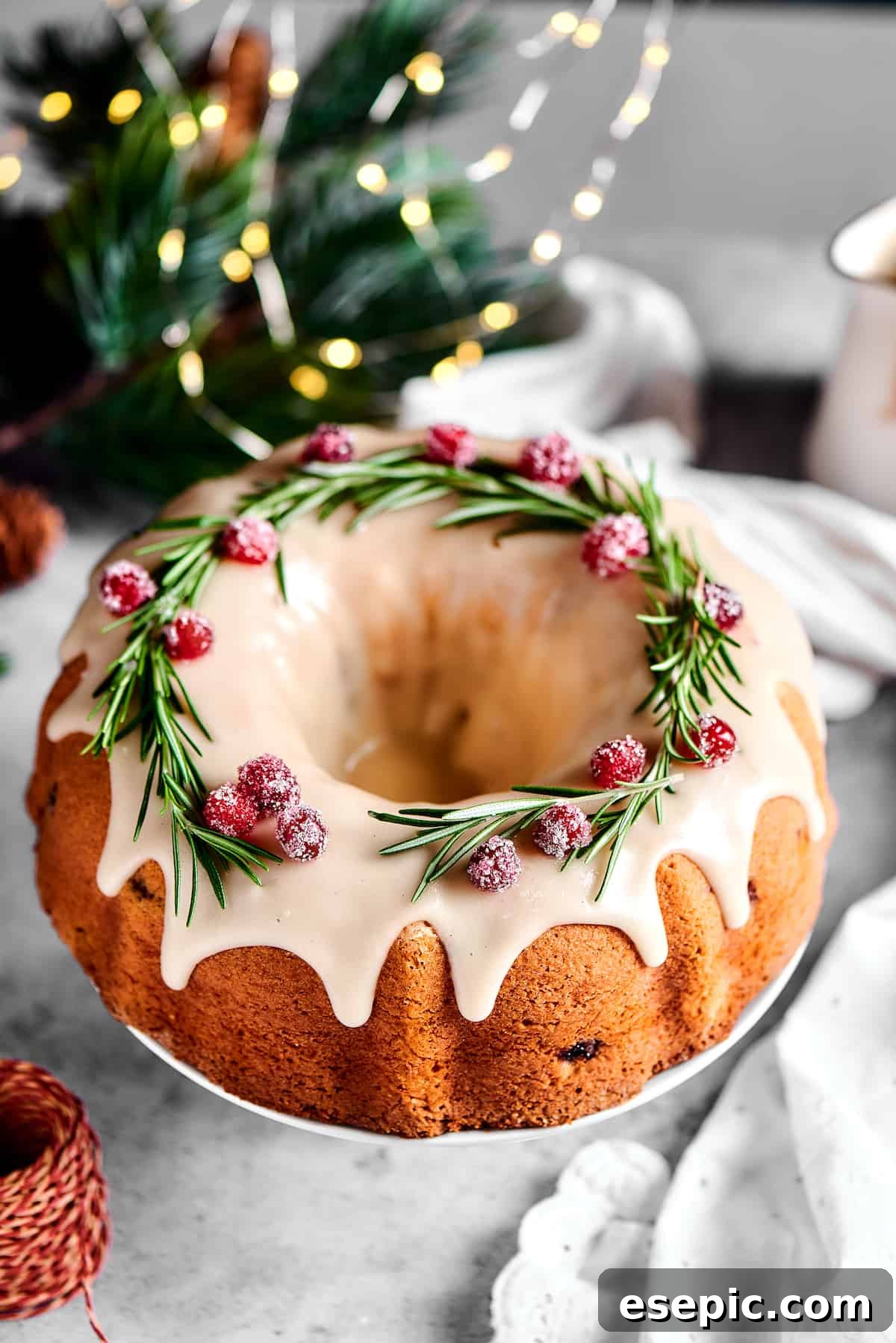 Christmas Cranberry Pound Cake is a festive holiday dessert with fresh cranberries, orange liqueur, vanilla bean paste, and a sweet glaze. An inviting overhead shot of the elegant Bundt cake, beautifully garnished with fresh rosemary sprigs and sparkling sugared cranberries, ready for serving.