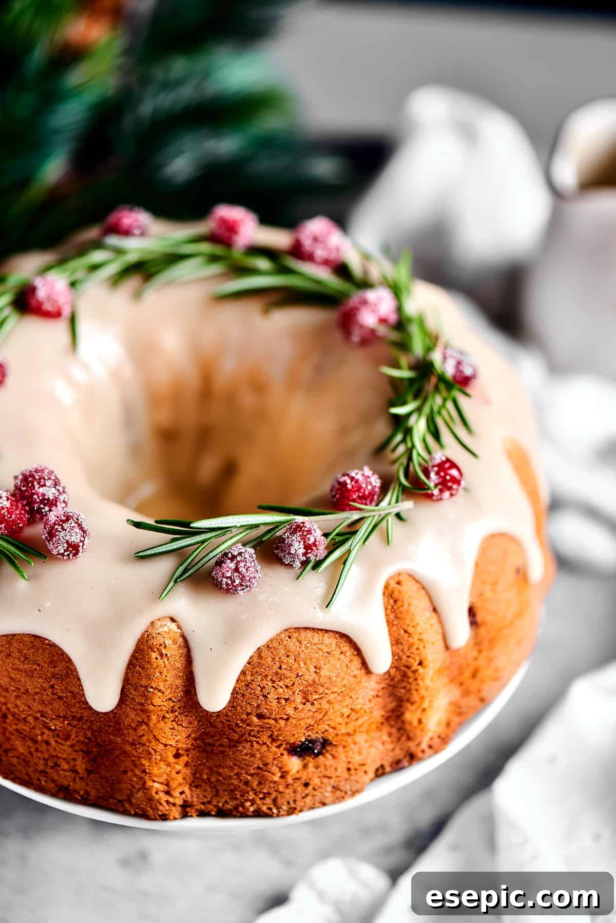 Christmas Cranberry Pound Cake is a festive holiday dessert with fresh cranberries, orange liqueur, vanilla bean paste, and a sweet glaze. A close-up, elevated view of the festive Bundt cake, highlighting the beautiful glaze and sparkling cranberry and rosemary garnishes, capturing the essence of holiday baking.