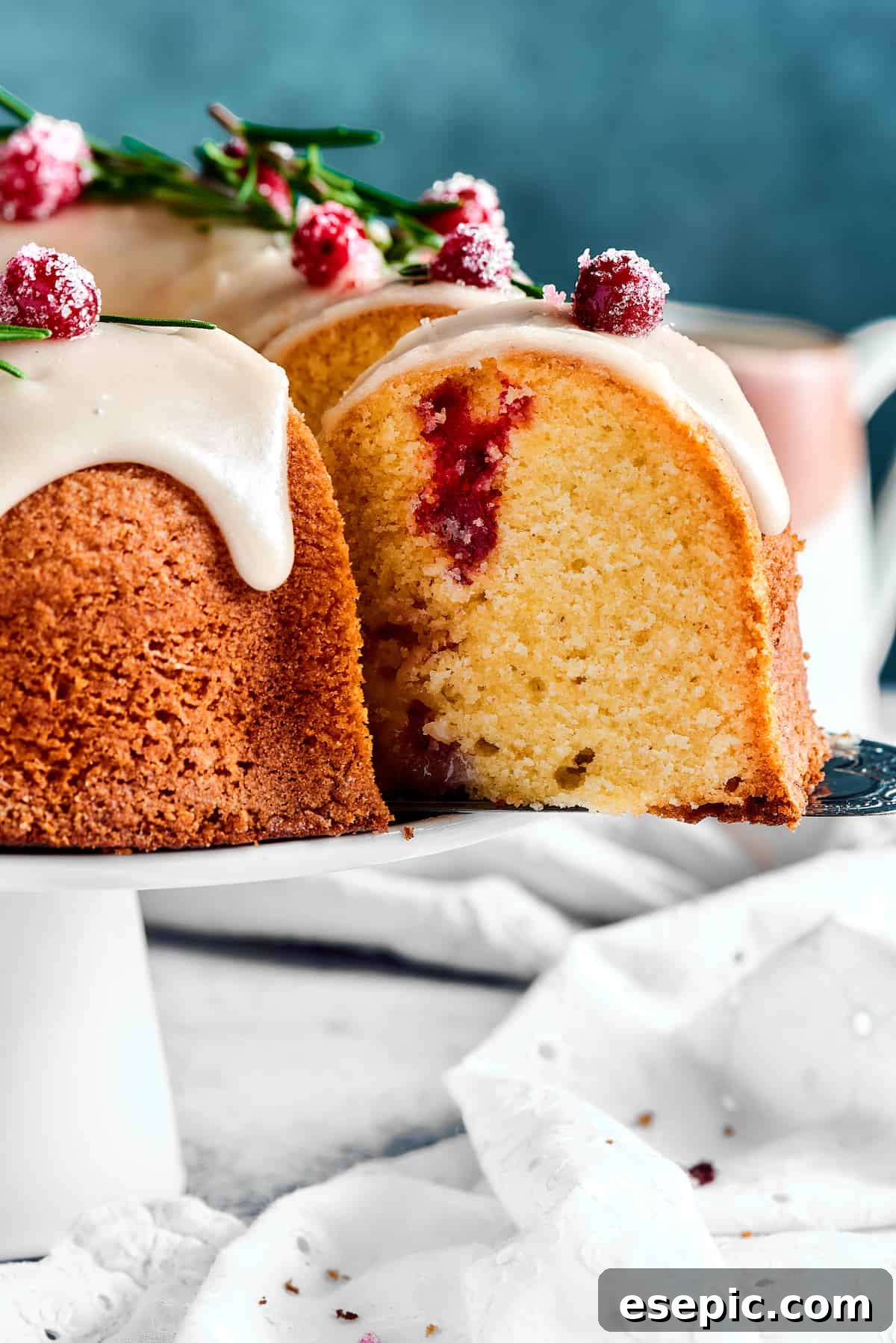 Christmas Cranberry Pound Cake is a festive holiday dessert with fresh cranberries, orange liqueur, vanilla bean paste, and a sweet glaze. A perfectly baked and glazed slice of pound cake being lifted from the cake stand with a cake server, ready to be savored.