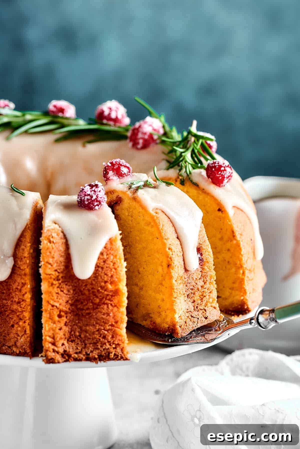 Christmas Cranberry Pound Cake is a festive holiday dessert with fresh cranberries, orange liqueur, vanilla bean paste, and a sweet glaze. A cranberry pound cake on a elegant cake stand, with a slice already removed, showcasing its moist texture and studded cranberries.