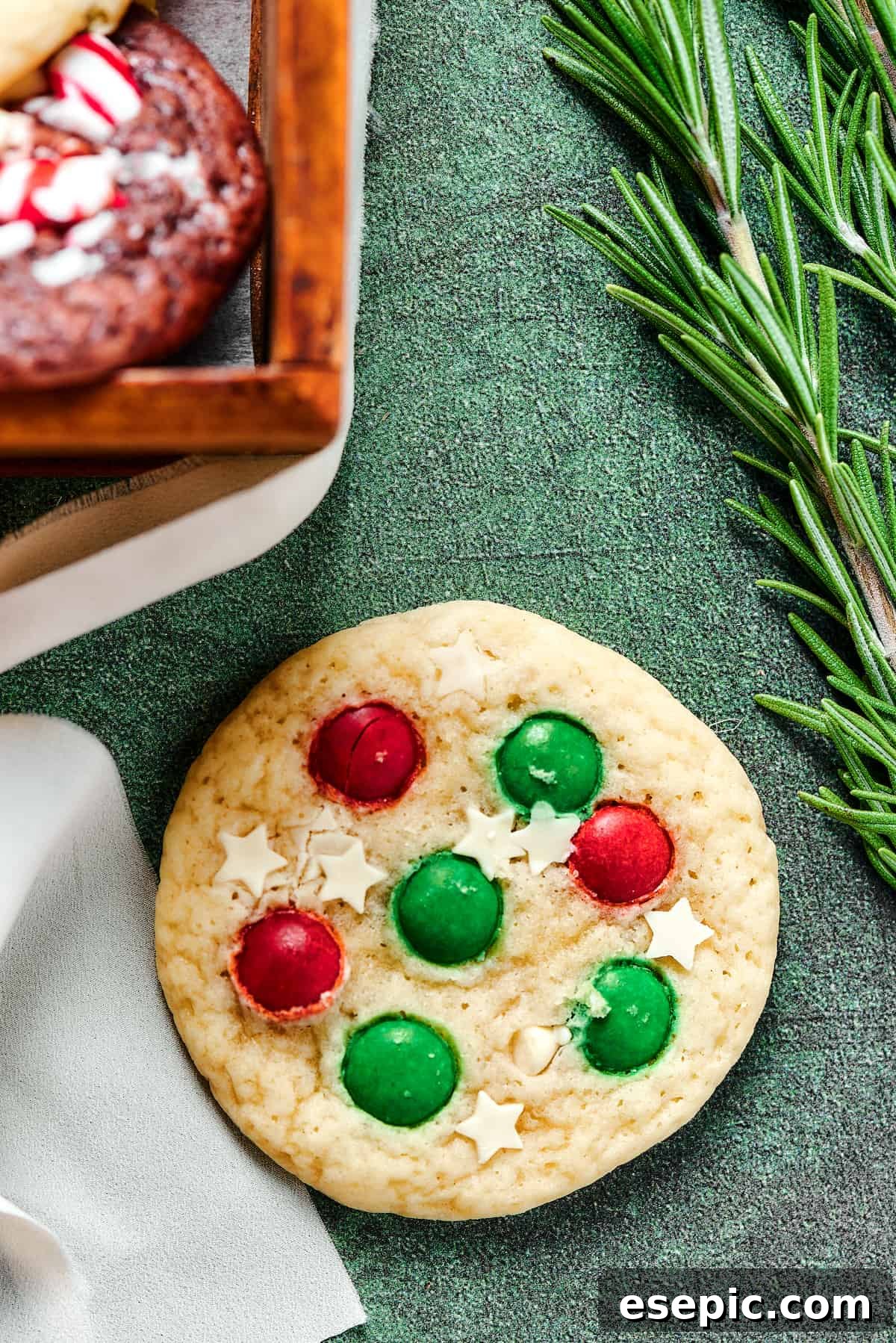 Easy vanilla and chocolate Christmas Cake Mix Cookies are studded with red and green M&Ms, and decorated with even more holiday goodies! A festive Christmas sugar cookie, elegantly decorated with delicate white chocolate stars and colorful M&Ms, resting on a white surface.