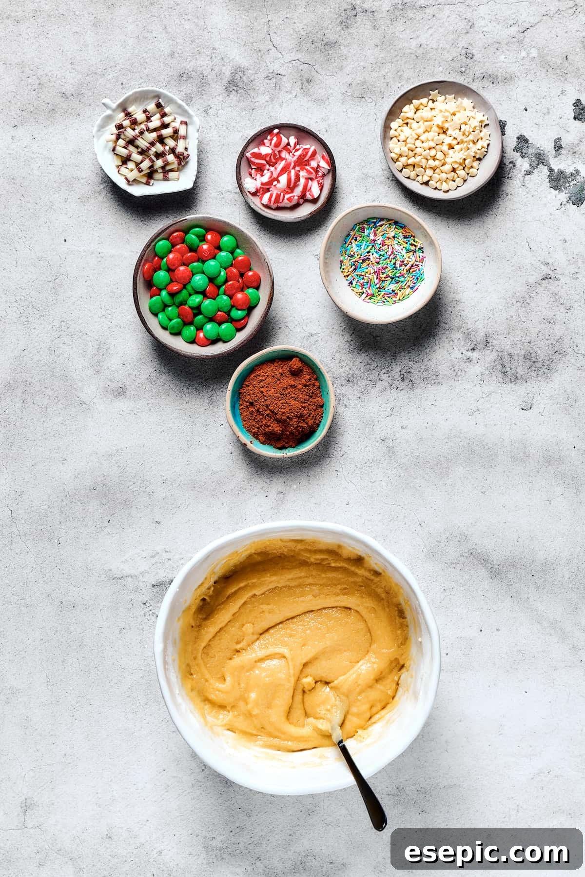Yuletide Cake Mix Wonders 4 A large bowl of thoroughly mixed cookie dough sits ready, surrounded by small, inviting dishes filled with various colorful cookie decorations.