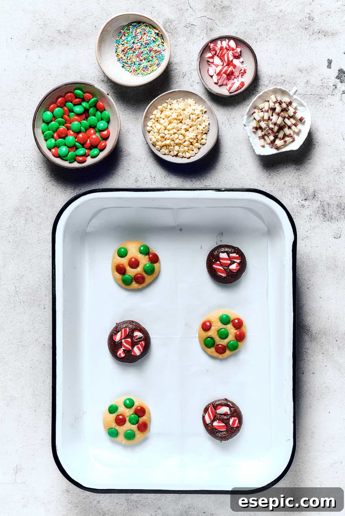 Easy vanilla and chocolate Christmas Cake Mix Cookies are studded with red and green M&Ms, and decorated with even more holiday goodies! An appetizing close-up of unbaked chocolate and vanilla cake mix cookies neatly arranged on a parchment-lined baking sheet, each generously studded with colorful M&M's pressed into the dough.