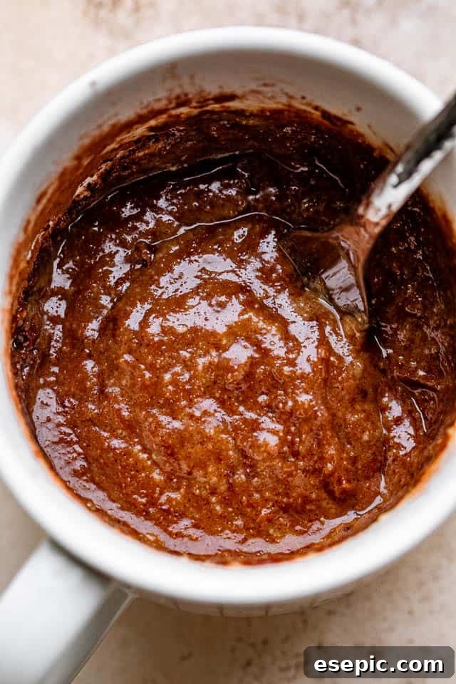 A fork stirring a rich chocolate batter inside a mug, combining all the ingredients smoothly.