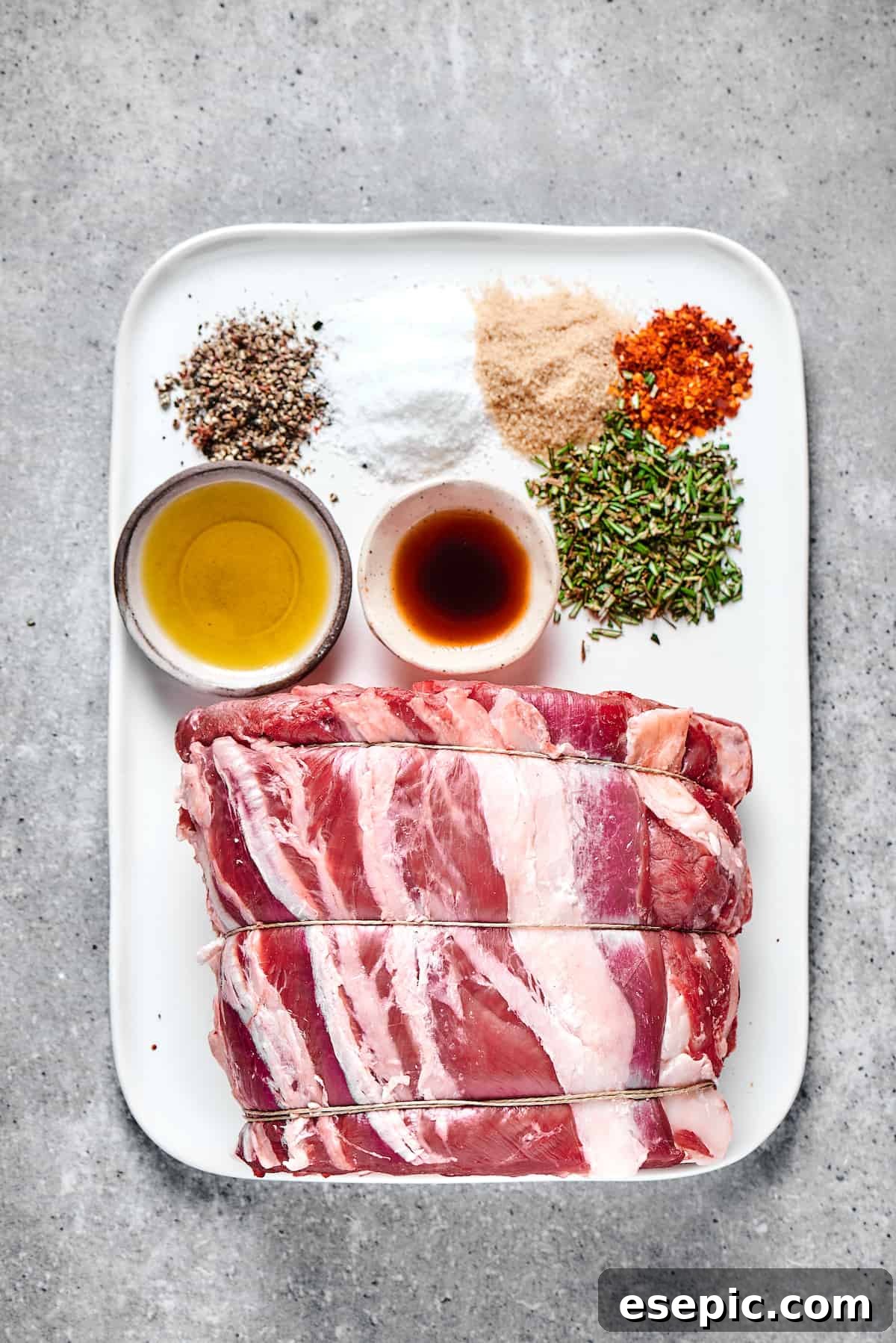 Raw prime rib roast on an enamel tray, seasoned and ready for roasting, alongside various spices and a bottle of Worcestershire sauce.