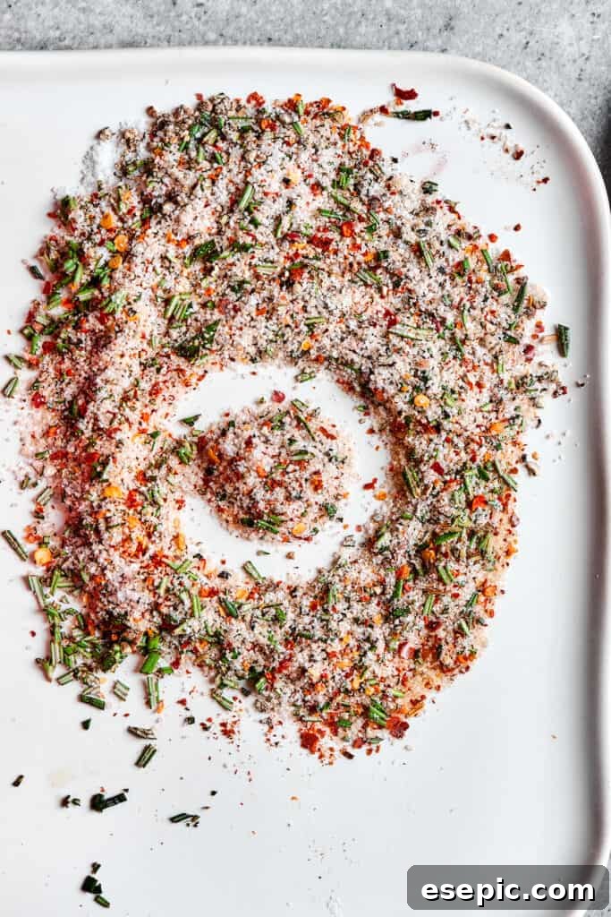 A vibrant blend of seasonings, including rosemary, chili flakes, and salt, artfully arranged on a tray.