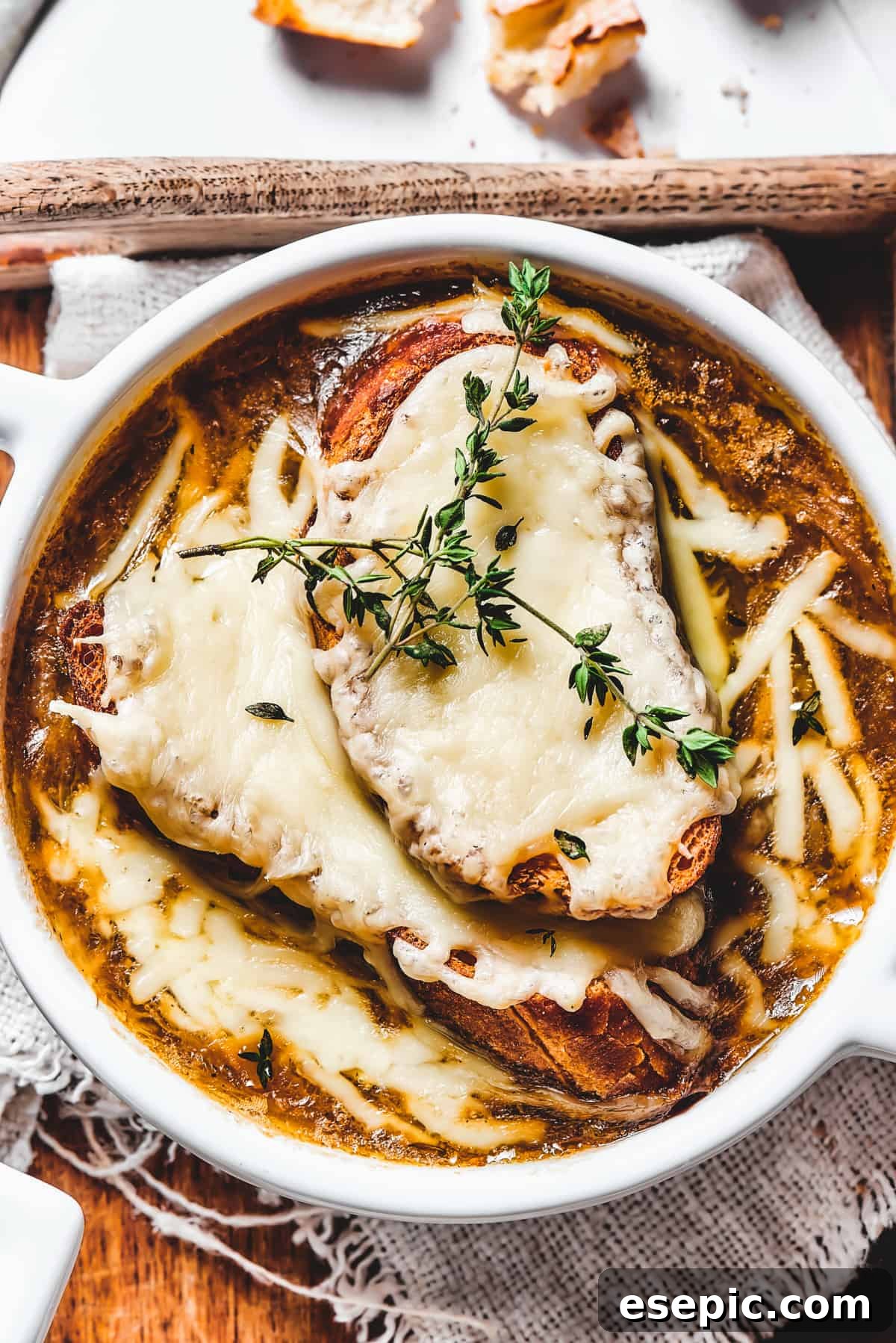 Overhead shot of rich French Onion Soup with bubbly melted cheese and fresh thyme garnish.