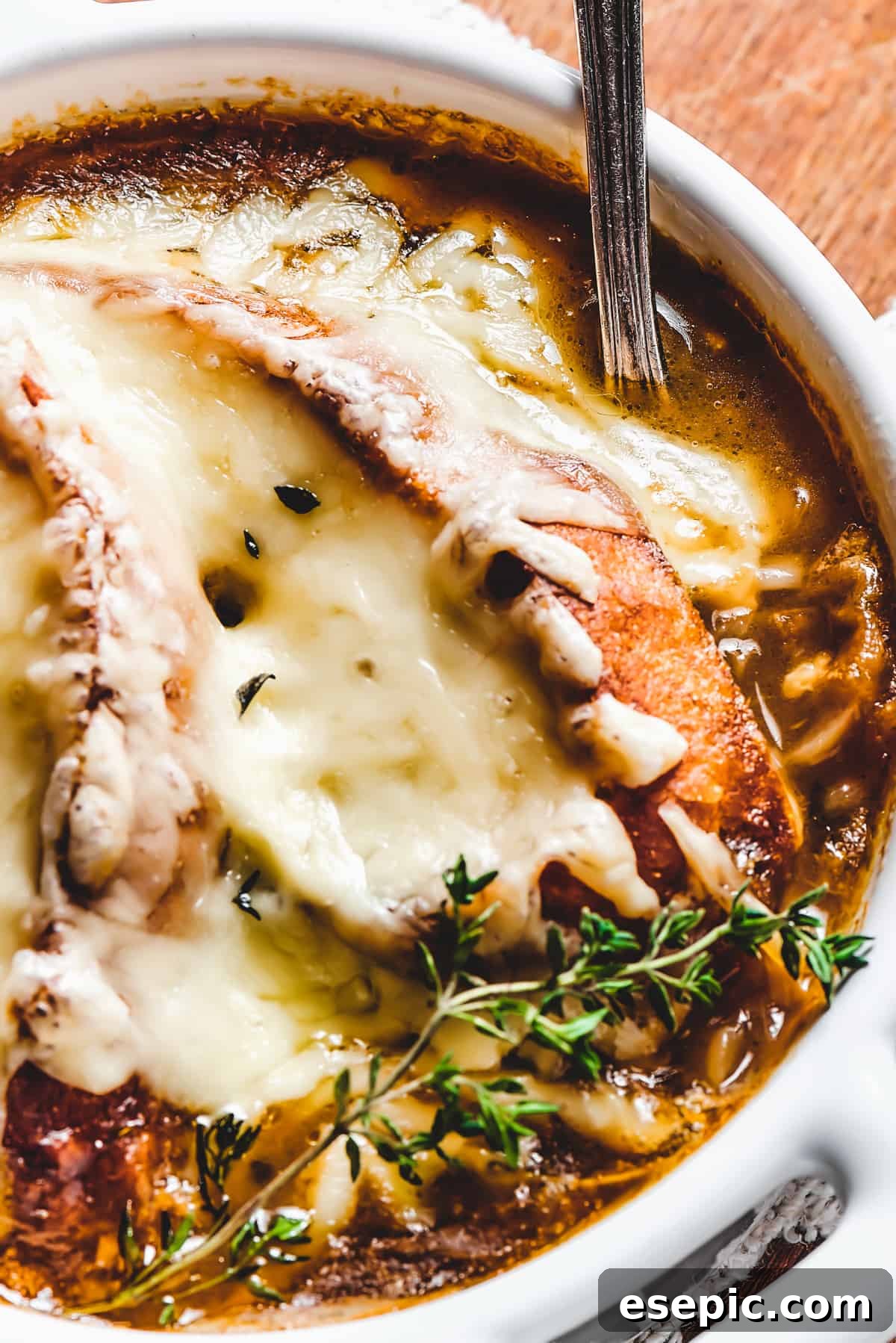 Close-up shot of French onion soup in a bowl, showcasing the rich brown broth, tender caramelized onions, and perfectly melted cheese, garnished with fresh thyme.