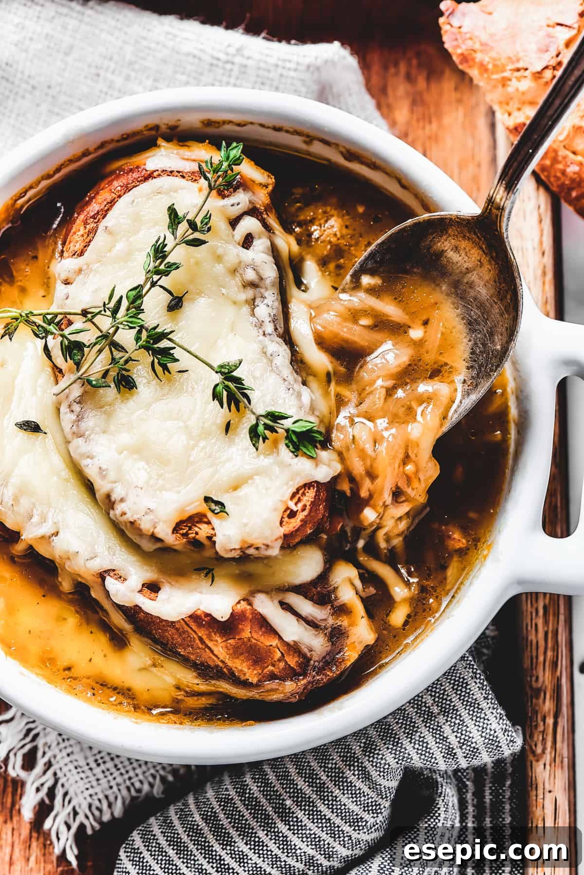 A person carefully spooning rich French Onion Soup from a rustic ceramic bowl, showcasing the tender onions and savory broth, ready to be enjoyed.