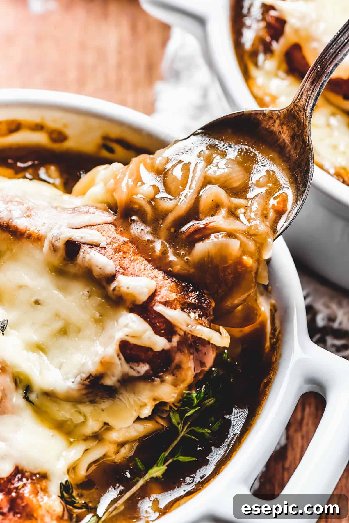 A person serving hot French Onion Soup from a large pot into an individual ceramic bowl with a ladle.