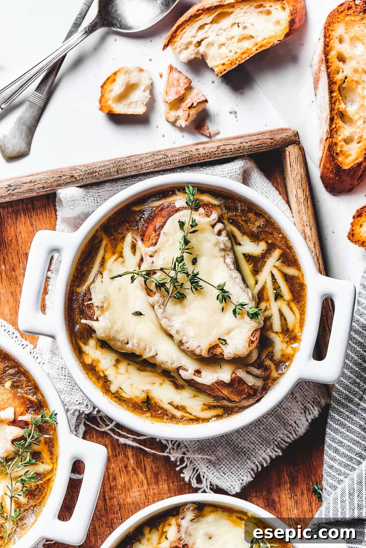 Double-handled ceramic bowls of French onion soup on a wooden tray, showing melted cheese and golden croutons, ready to be served.