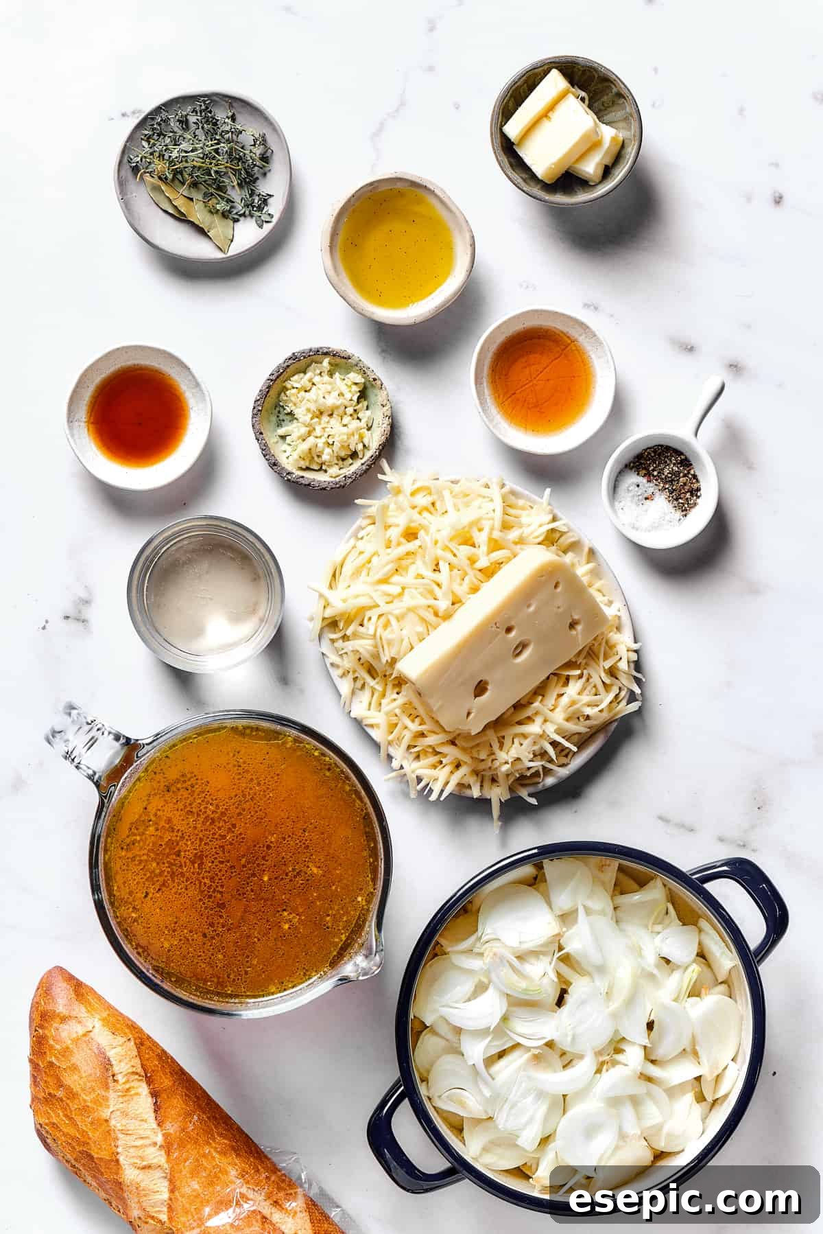 Arrangement of fresh ingredients for French Onion Soup on a rustic wooden surface: yellow onions, minced garlic, fresh thyme, bay leaves, white wine, beef stock, butter, and a variety of shredded cheeses.