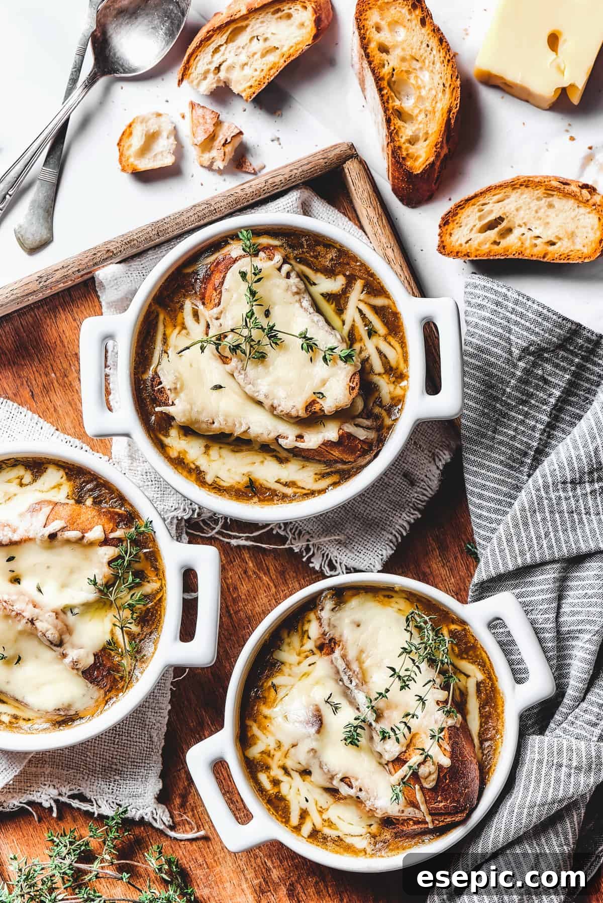 Individual oven-safe bowls of French onion soup topped with perfectly melted and bubbly cheese croutons, garnished with fresh herbs, ready for serving.