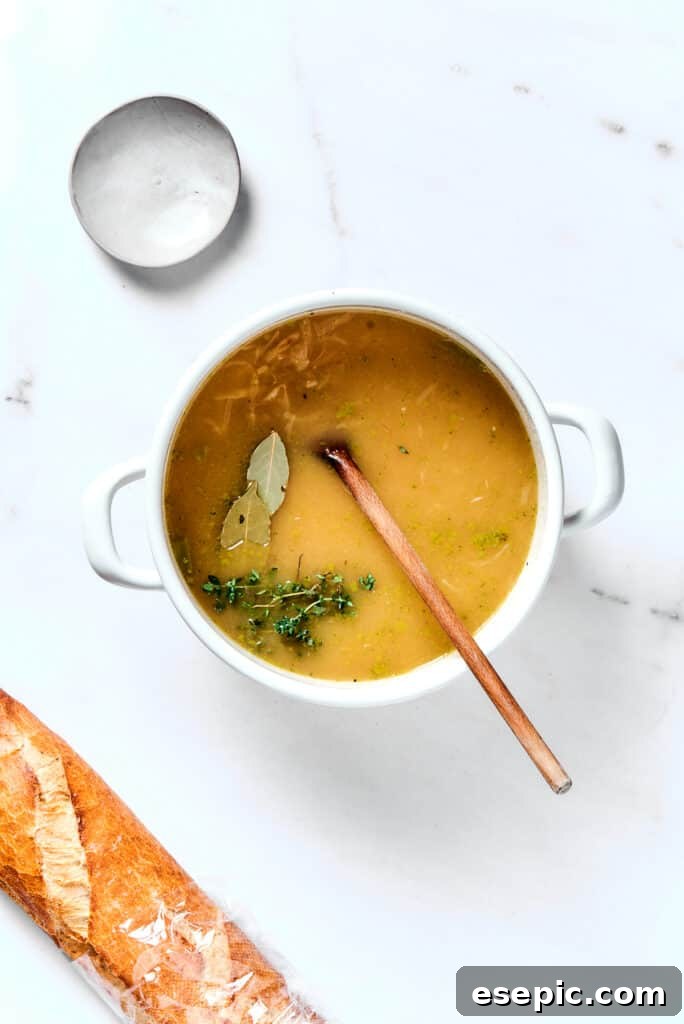Close-up view of French onion soup simmering in a large pot, showing the rich brown broth, tender onions, and the herbs infusing their flavor.