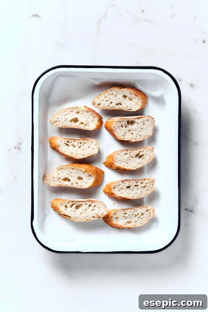 Slices of French baguette arranged neatly on a baking sheet, ready for toasting in the oven to create crisp croutons.