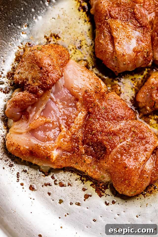 Raw chicken thighs generously coated with a dark Cajun seasoning rub, ready for pan-searing.