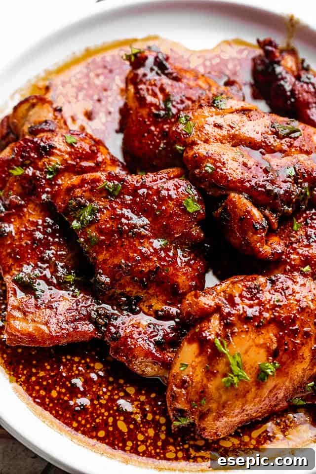 Two beautifully pan-seared Cajun butter chicken thighs on a white plate, drizzled with sauce and garnished with parsley.