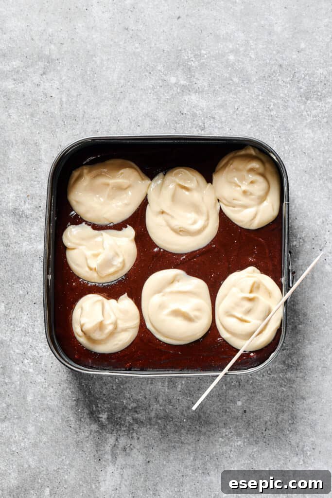 Dollops of white cream cheese mixture on a dark brownie batter in a baking pan.