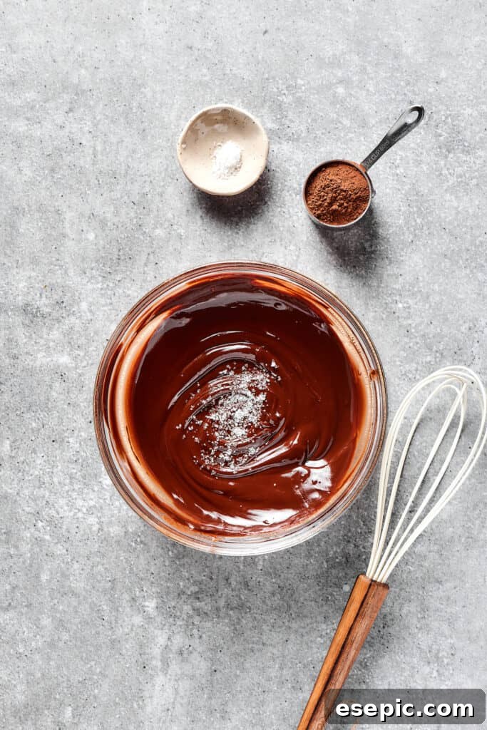 A bowl of melted butter and chocolate, with cocoa powder and salt nearby on a white surface.