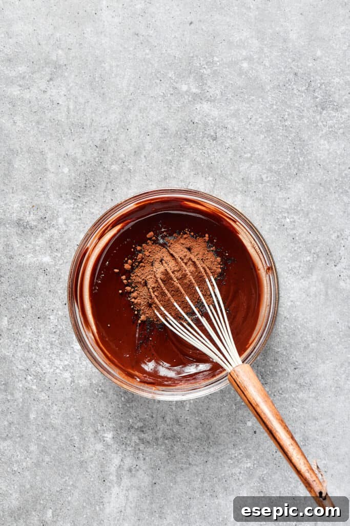 A whisk incorporating cocoa powder into a rich, dark brownie batter in a mixing bowl.