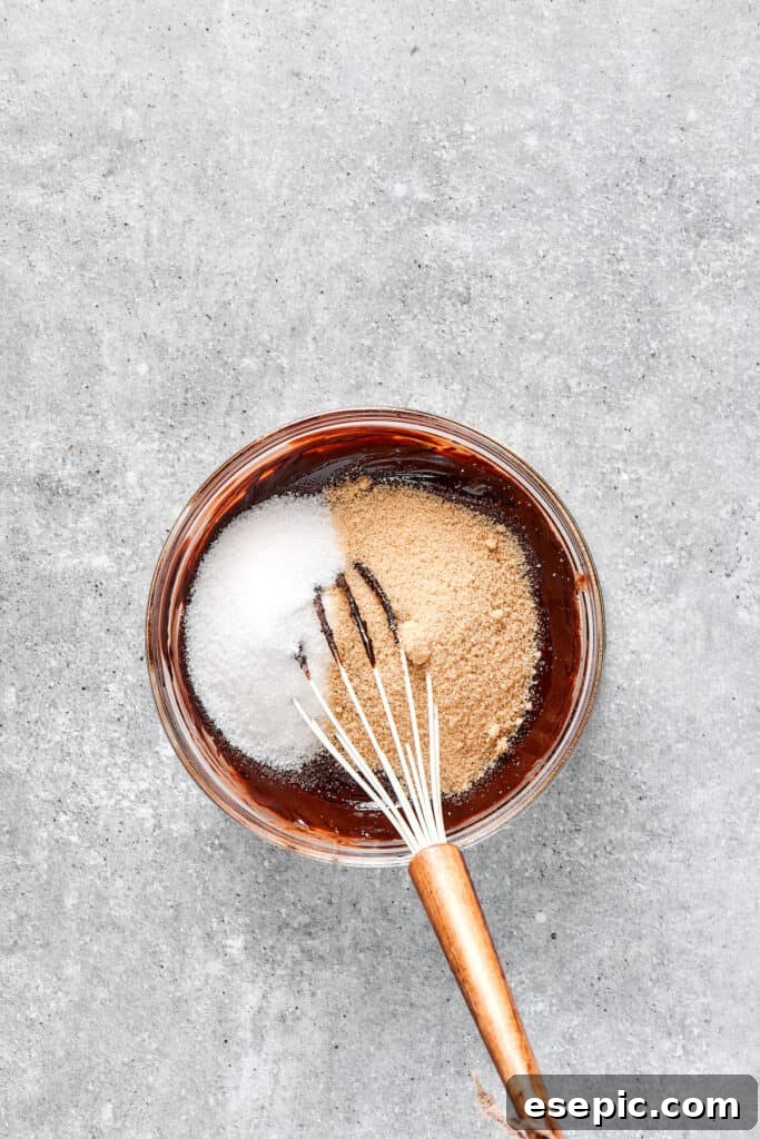 A hand whisking granulated sugar into the dark, melted chocolate and butter mixture.