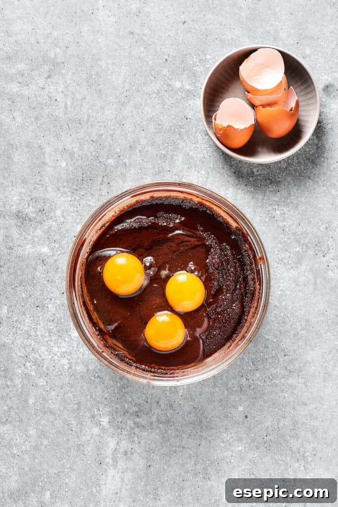 Adding an egg to the brownie batter, which is being mixed in a bowl.