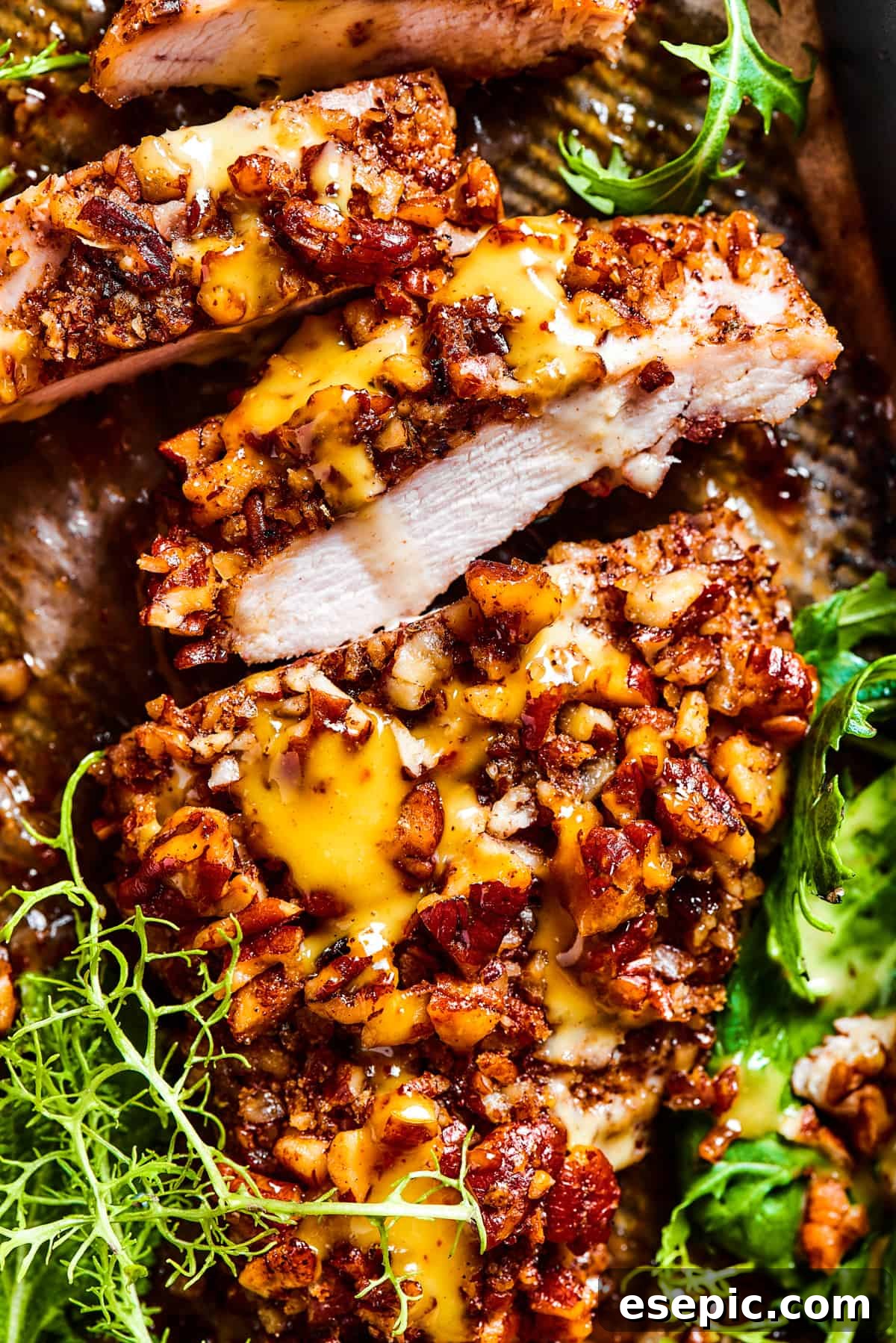 Sliced pecan chicken on a serving dish, with greens placed around the chicken.