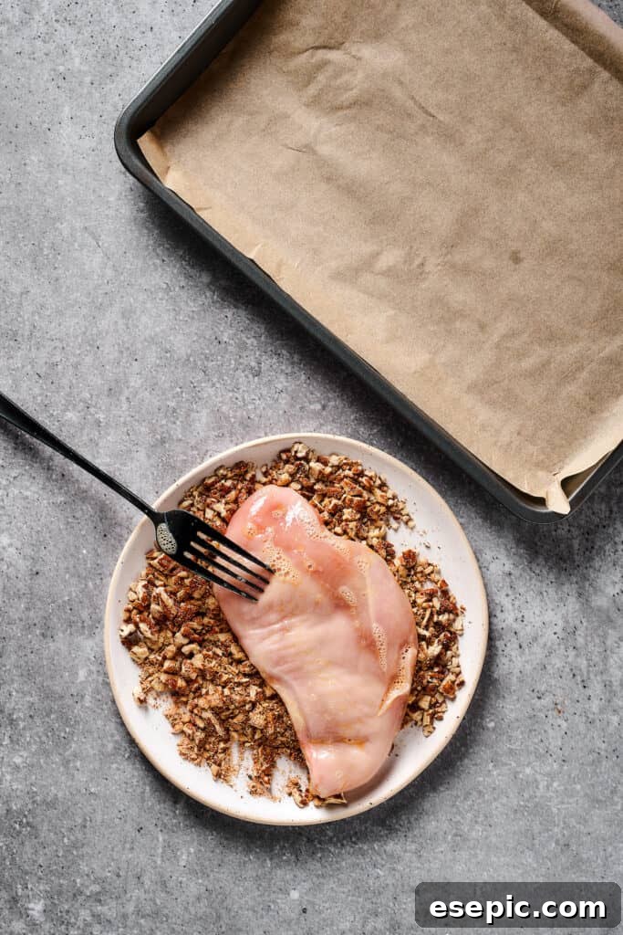 Raw chicken being coated in a ground pecan mixture.