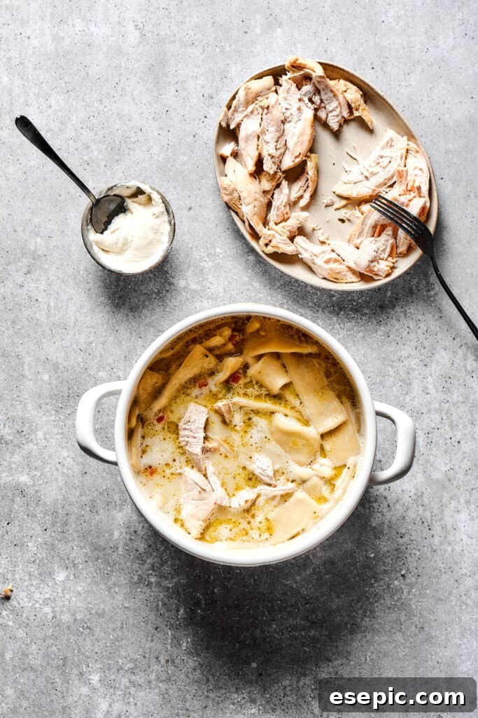 Simple Comfort Chicken and Dumplings 8 Flat dumplings cooked in soup next to a plate of shredded white meat and a measuring cup of thick cream.