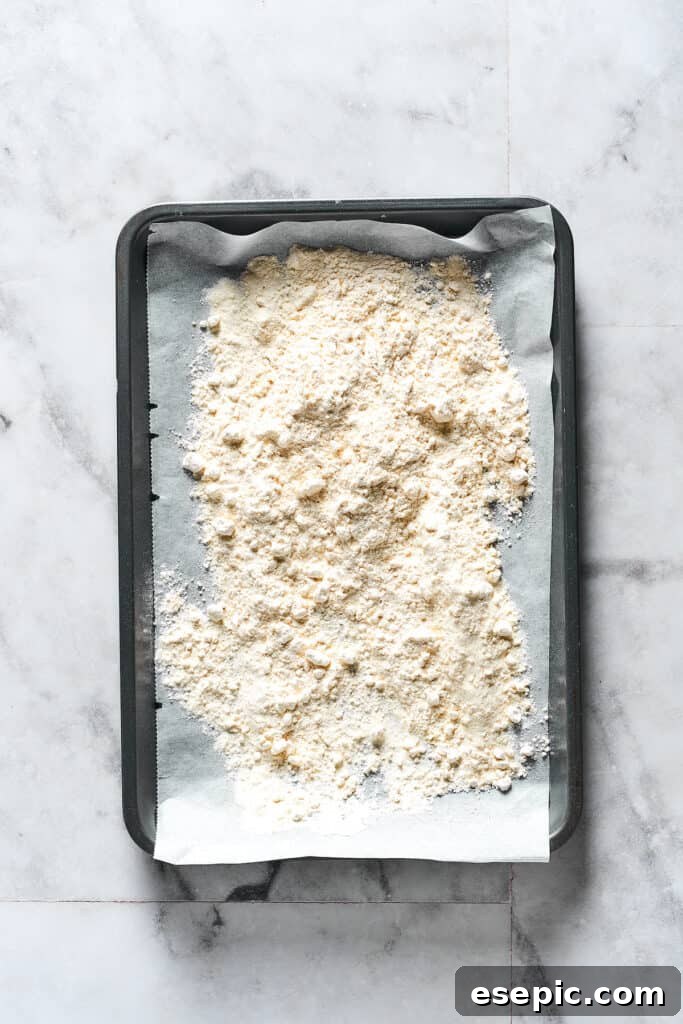 Flour spread out on a parchment-lined baking sheet, ready for heat treatment.