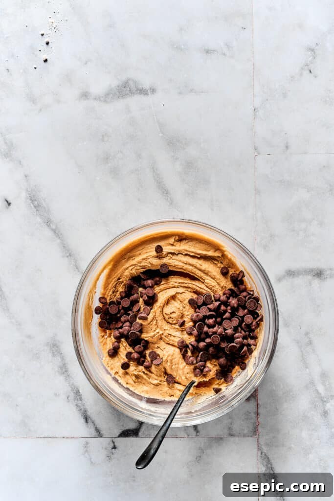 Adding chocolate chips to the prepared cookie dough, ensuring even distribution.