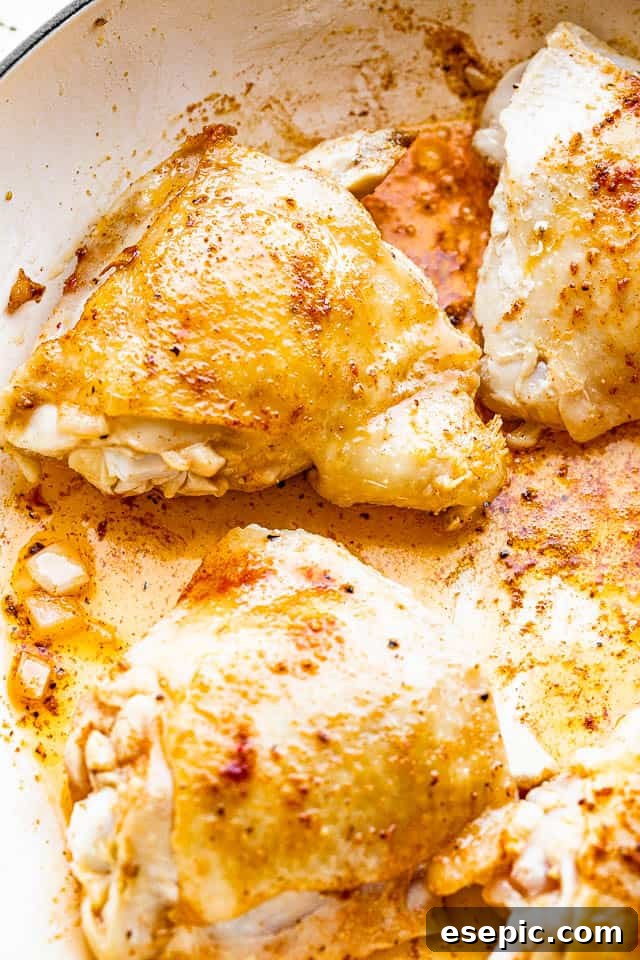 Close-up of chicken thighs sizzling and browning in an oven-safe skillet on the stovetop.