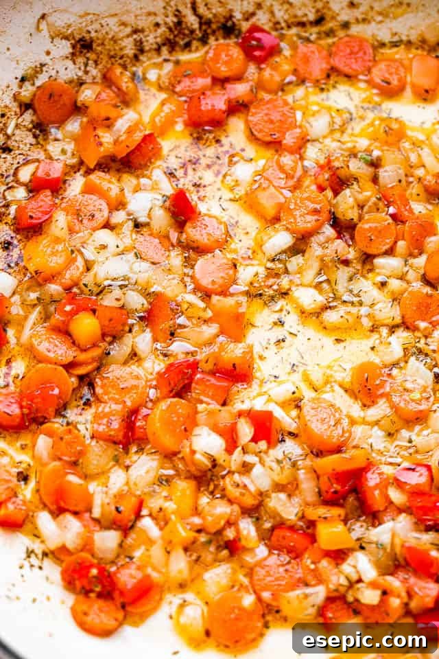 Colorful diced carrots, red bell peppers, and onions sautéing in butter in a white skillet, releasing their sweet aromas.