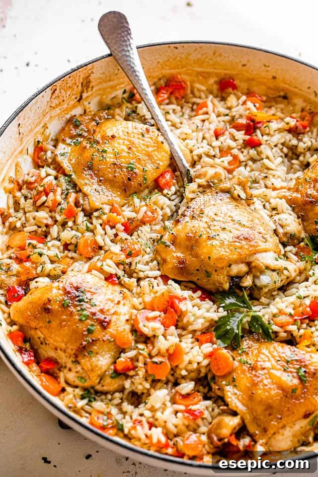 A large white skillet filled with savory one-pot chicken and rice, featuring browned chicken thighs and colorful vegetables, ready to be dished out.