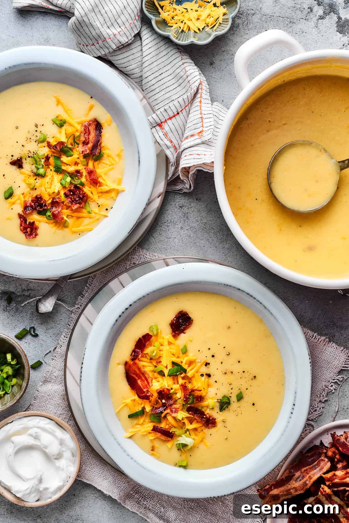 A large soup pot filled with creamy baked potato soup, positioned alongside two perfectly garnished bowls of the same soup, inviting a delicious meal.